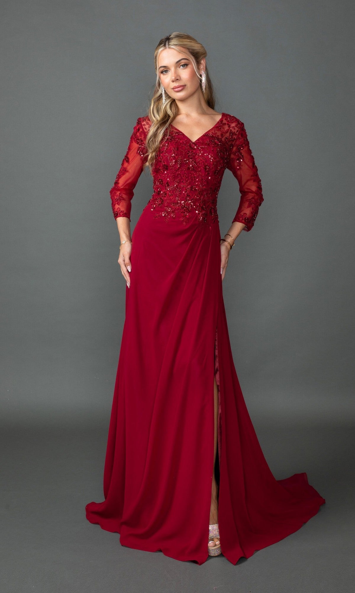 A woman models the Dancing Queen 4543 long formal dress, featuring a deep red A-line skirt, sheer embellished sleeves, and a V-neckline against a plain gray background.